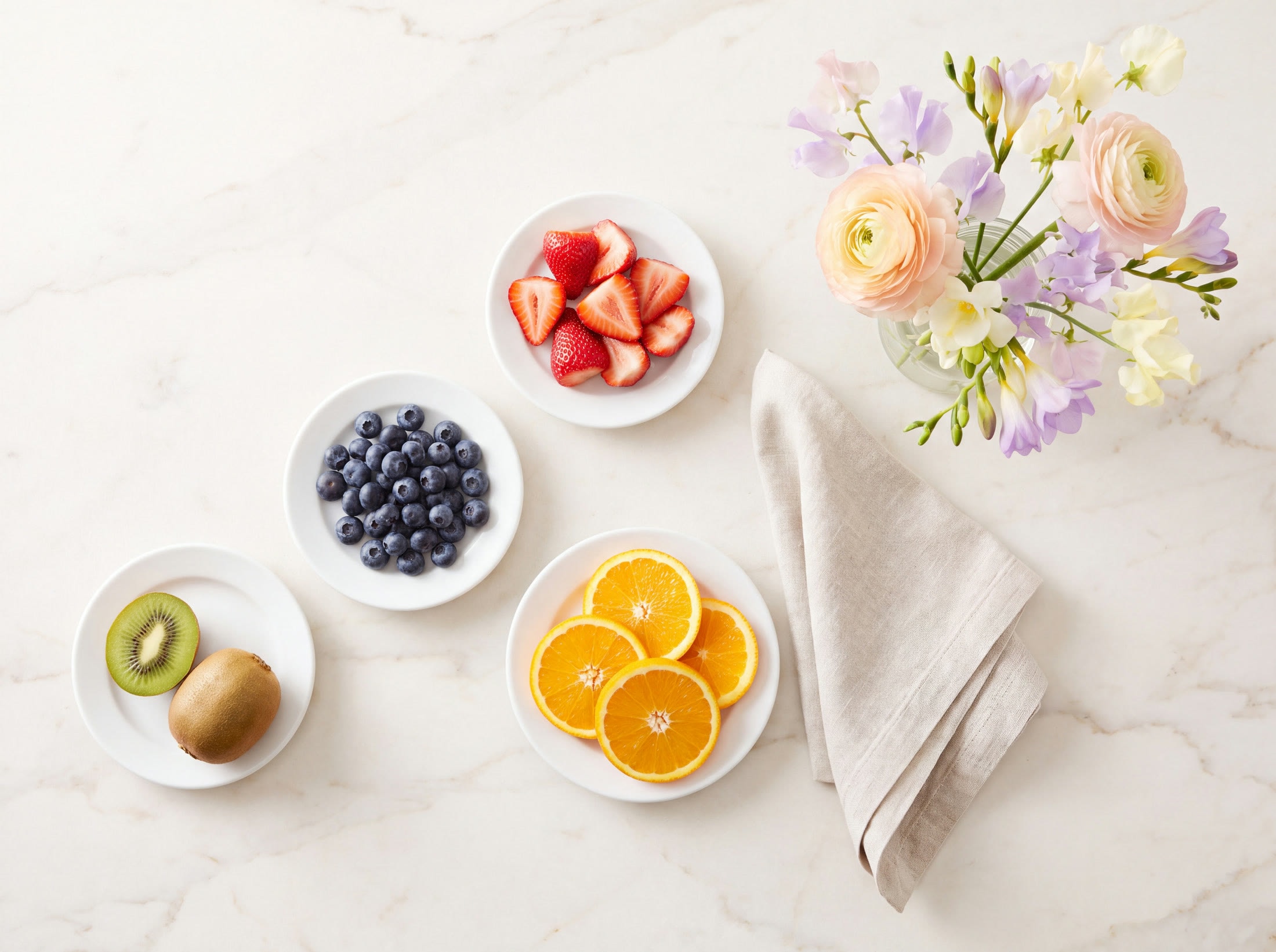 An overhead arrangement of plates, fruit and flowers on pale marble